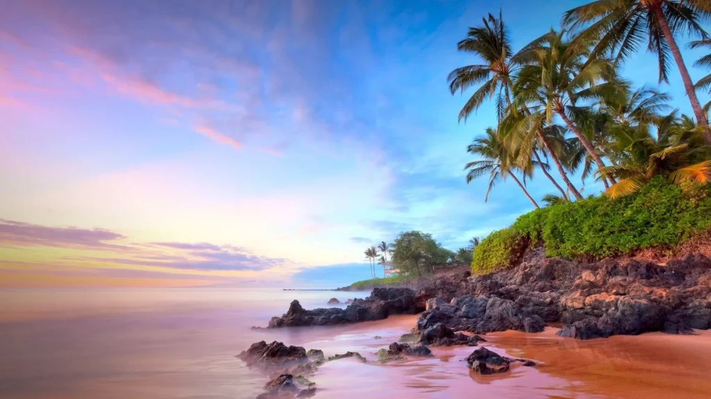 A scenic tropical beach in Hawaii at sunset with palm trees, ocean waves, and a rocky shoreline is perfect for outdoor activities in Hawaii, such as beach exploration and coastal hikes.