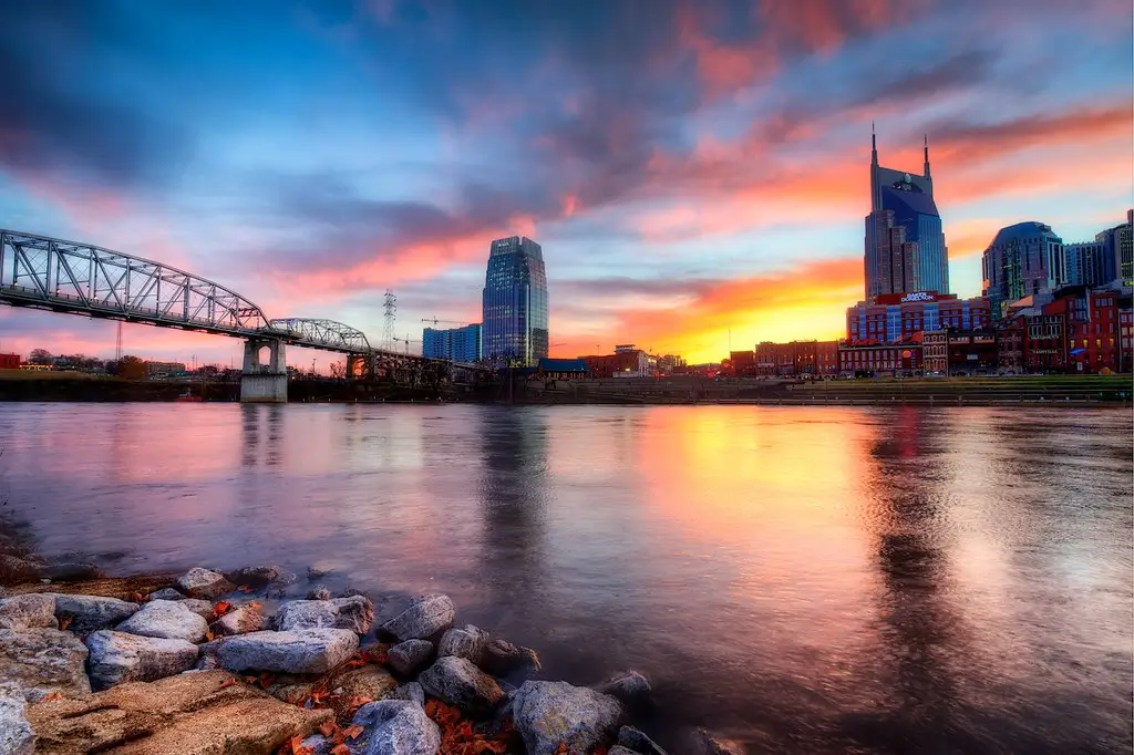 Sunrise over Nashville Tennessee, with the John Seigenthaler Pedestrian Bridge spanning the Cumberland River, reflecting vibrant pink and orange hues in the water. Top hidden gems in Nashville TN.